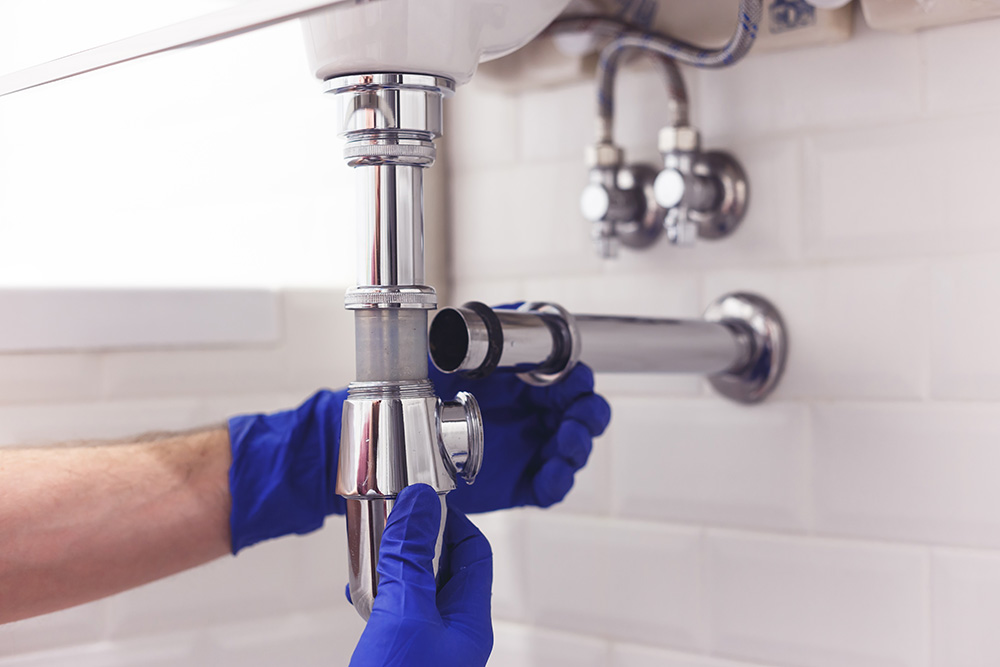 Plumber repairs and maintains chrome siphon under the washbasin. Plumber at work in bathroom, plumbing assemble and install concept