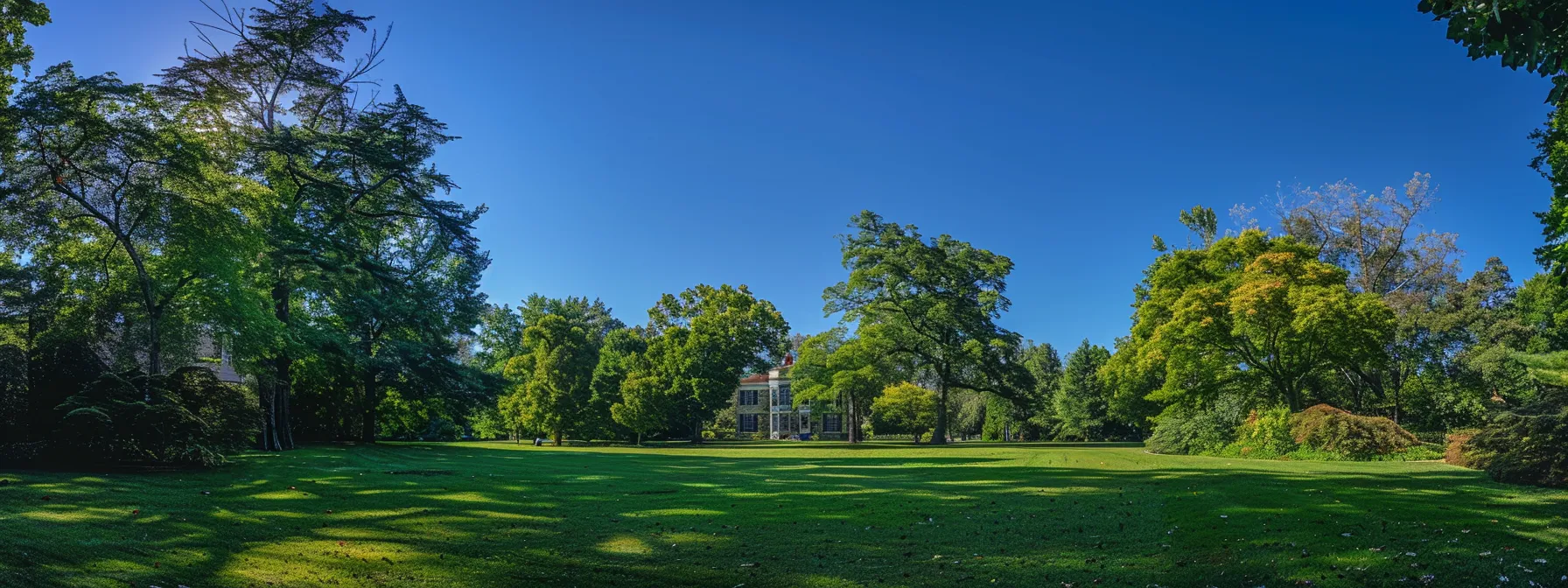 a historic colonial-era mansion surrounded by lush green gardens and towering oak trees under a clear blue sky in litchfield, ct.